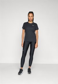 Sort sports t-shirt med ribbet tekstur, parret med glinsende sorte leggings. Begge dele har et lille logo. Båret med sorte sportsko.