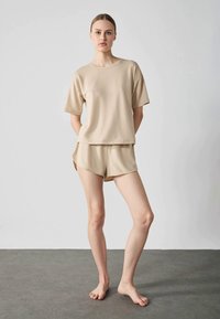 Beige bomullsloungewear-set bestående av en kortärmad topp och shorts. Shorts har sidoklyftor och en avslappnad passform, med en mjuk textur.