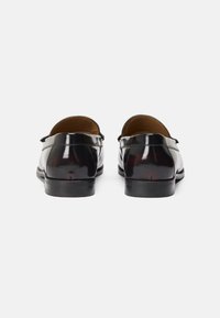Chaussures en cuir verni noir avec une finition lisse, des talons bas et arrondis, et un design classique de mocassins. Accents de piqûres subtiles sur les bords.