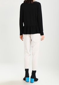 Maglietta nera a maniche lunghe con dettaglio peplum, abbinata a pantaloni bianchi a righe e stivaletti neri alti fino alla caviglia con tacco blu.