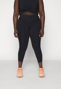 Top deportivo negro de tirantes con un detalle anudado, combinado con leggins negros ajustados. El calzado presenta acentos en rosa claro, naranja y amarillo.