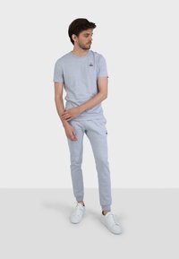 T-shirt in cotone grigio e pantaloni sportivi coordinati, con un piccolo logo sulla maglietta, design aderente e polsini a coste. Sneakers bianche.