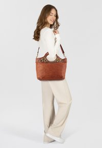 Borsa a tracolla in pelle marrone con una forma strutturata, caratterizzata da perline decorative e colorate lungo il bordo superiore.