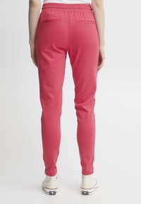 Pink jogger pants with an elastic waistband, two back pockets, and a slim fit, paired with white high-top sneakers. Smooth fabric texture.