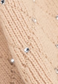 Beige gebreide trui met een gestructureerd patroon, voorzien van glimmende zilveren strass steentjes verdeeld over het geheel als decoratieve accenten.