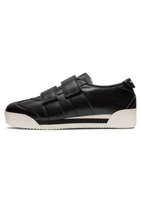 Baskets basses noires avec deux larges bandes Velcro et une semelle en caoutchouc blanche avec une bande noire.