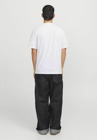 Witte T-shirt met korte mouwen gecombineerd met donkere spijkerbroek. De spijkerbroek heeft een rechte pasvorm en opgerolde mouwen, wat een klassiek ontwerp benadrukt.
