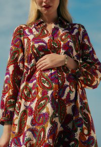 Bunt gemustertes Kleid mit Paisley-Muster und lebendigen roten, grünen und lila Akzenten. Der Stoff ist leicht und hat eine lässige Passform sowie Knopfdetails.