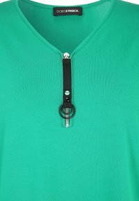 Green short-sleeved top with a zippered collar, featuring a black zipper tab, round accent, and a smooth, lightweight fabric texture.