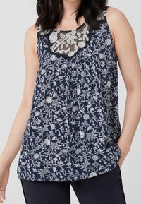 Granatowa bezrękawnik z białym kwiatowym wzorem, z koronkowym dekoltem. Miękka tkanina z luźnym krojem i okrągłym dołem.