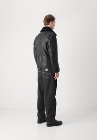 Musta nahkatakki, jossa on turkistakki, yhdistetty tummiin farkkuihin, joissa on näkyvät saumat ja logo-tasku takana.