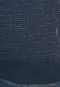 Marineblaues Sweatshirt mit strukturiertem Muster, geripptem Saum und Bündchen sowie einer Kängurutasche auf der Vorderseite, die dezente weiße Sprenkel aufweist.