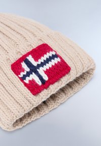 Gebreide beige beanie met een brede ribbelstructuur en een rechthoekig Noors vlagpatch in rood, blauw en wit aan de voorkant.