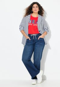 Randig blazer, röd t-shirt med grafik och text, samt mörkblå vida jeans med fickor. Vita sneakers fulländar outfiten.