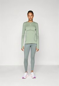 Ilgas rankovėmis šviesiai žalia sportinė palaidinė su kūno kontūrų dizainu, derinama su atitinkančiomis aptemptomis tamprėmis ir baltais sportbačiais su rožiniais akcentais.