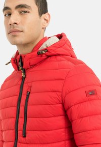 Rote Pufferjacke mit gestepptem Design, ausgestattet mit einer Kapuze, Reißverschluss und einem kontrastierenden Innenfutter. Schwarzer Reißverschluss und Logodetail.