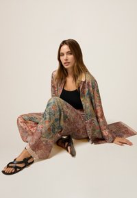 Set di tessuti leggeri a fantasia floreale composto da una camicia a maniche lunghe e pantaloni a gamba larga in morbidi colori pastello, abbinato a sandali neri.
