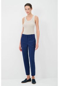Beige geribde tanktop gecombineerd met strakke marineblauwe broek, gemaakt van soepele stof en met een enkellange snit, aangevuld met donkere loafers.