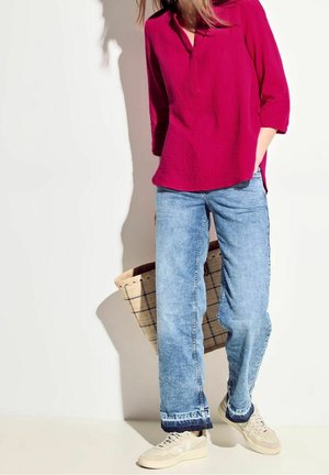 Haut en coton cramoisi avec col, manches trois-quarts ; associé à un jean en denim bleu clair à coupe décontractée ; baskets blanc cassé ; sac fourre-tout en paille tressée.