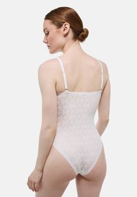Body en dentelle blanche avec motif floral, bretelles spaghetti réglables et une coupe haute. Texture douce avec une apparence transparente.