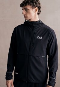 Μαύρο ελαφρύ μπουφάν με φερμουάρ μπροστά, κουκούλα και λογότυπο EA7. Διαθέτει ανακλαστικές λεπτομέρειες και απαλή, ματ υφή.