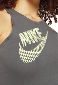 Szary sportowy top na szerokich ramiączkach z dużym, żółtym, kropkowanym logo Nike na piersi. Gładka tekstura materiału.