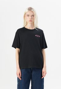 T-shirt noir à manches courtes avec un col rond et un détail de logo rose sur la poitrine gauche. Fabriqué en tissu en coton lisse.