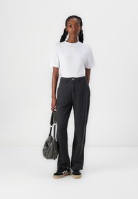 T-shirt blanc à manches courtes, pantalon noir ample avec poches, baskets noires avec semelles beiges et un sac à épaule gris foncé.