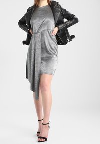 Robe argentée métallique avec un ourlet asymétrique, portée sous une veste en cuir noir cloutée. Des talons noirs à lanières complètent le look.
