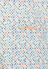 Katoenen stof met een witte achtergrond, gekenmerkt door een veelkleurig stippenpatroon in blauw, groen, oranje en rood. Bevat een geborduurd logo in beige.