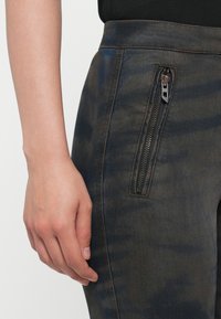 Dark denim trousers feature a side zip pocket. The fabric displays a subtle tie-dye pattern with shades of blue and grey, and contrasting stitching.