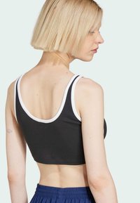 Zwarte crop top met witte rand, zachte katoenen stof, ronde halslijn en smalle bandjes; gedragen met blauwe shorts met elastische taille.