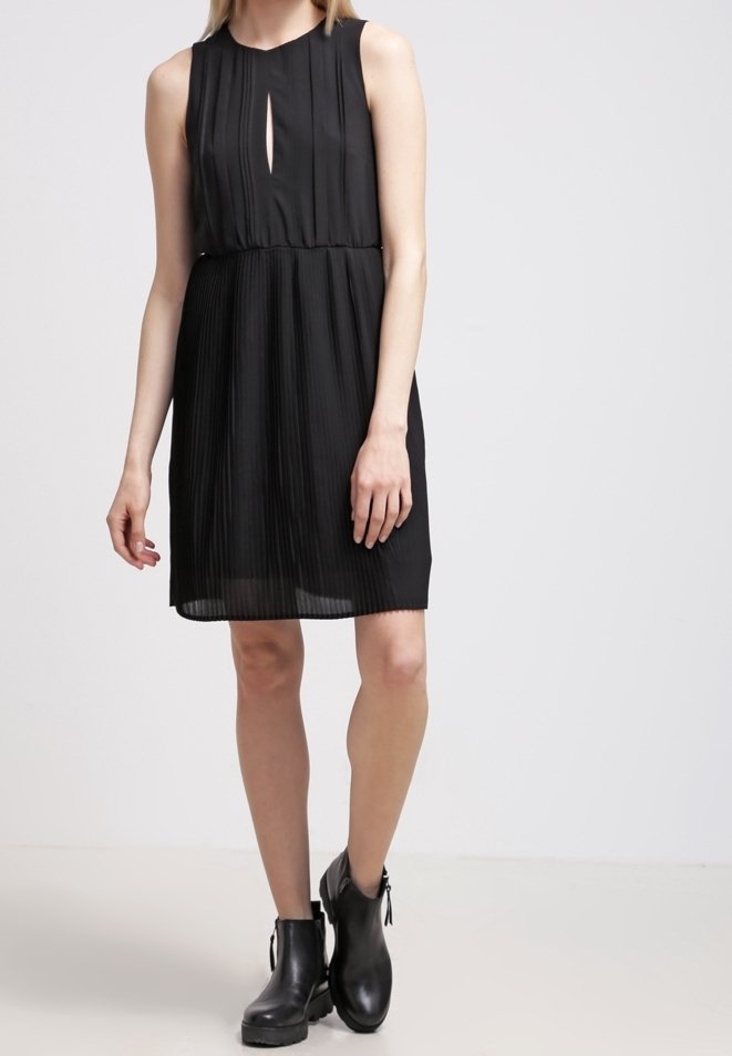 Černé skládací šaty s výstřihem ve tvaru klíče, bez rukávů a s upnutým pasem, doplněné černými kotníkovými botami. Hladká textura látky.