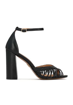 Sandale negre cu toc înalt și gros, cu barete împletite și o curea la gleznă cu o cataramă aurie. Textură netedă din piele.