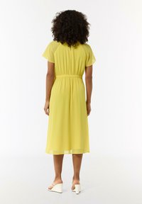 Gelbes Midi-Kleid mit kurzen Ärmeln, taillierter Taille und fließendem Saum. Glatter, leichter Stoff mit subtiler Transparenz.