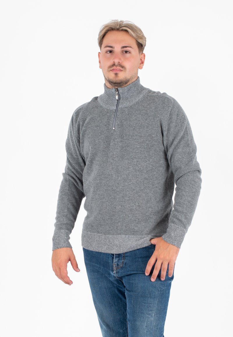 Maglione grigio con zip e colletto alto realizzato in un morbido tessuto a maglia, con polsini e bordo a coste, abbinato a jeans in denim blu.