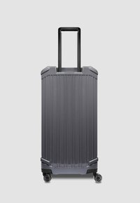 Hartschaliges graues Gepäckstück mit vertikalen Rillen, ausziehbarem schwarzem Griff und vier Rollen für Mobilität. Verfügt über abgerundete Ecken und verstärkte Kanten.