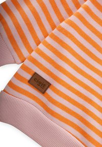 Dettaglio di un maglione a righe arancioni e rosa con polsini a coste e un'etichetta in pelle del marchio. Tessuto liscio, vestibilità regolare.