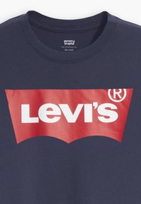 Sötétkék pamut póló, amelyen egy nagy piros Levi's logó látható fehér szöveggel, ívelt zászlóformában az elején. Kerek nyakú kivitel.