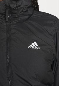 Giacca nera con zip realizzata in materiale liscio e imbottito. Presenta un collo alto e il logo Adidas bianco sul lato sinistro.