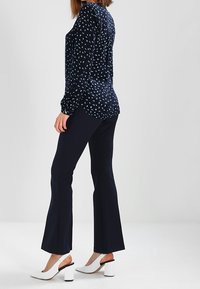 Blouse navy avec un petit motif bleu clair, associée à un pantalon évasé navy et des talons blocs blancs. Tissu lisse, coupe décontractée, détails minimaux.