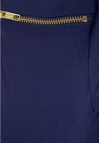 Námořnická tkanina s hladkým povrchem vyniká zvýrazněným zlatým zipem podél švu, který poskytuje kontrastní metalický akcent.