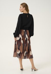 Black long-sleeve blouse with puffed shoulders, paired with a pleated skirt featuring abstract brown, white, and gray patterns.