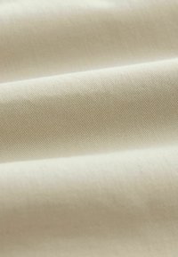 Tejido beige con una textura suave, que presenta un sutil estriado diagonal. La superficie muestra un fino patrón de tejido, lo que realza la durabilidad.