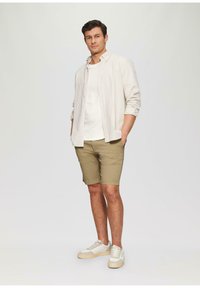Kevyt, raidallinen nappikauluspaita valkoisen T-paidan päällä, yhdistettynä khakivärisiin shortseihin ja valkoisiin tennareihin, joissa on vaaleanbeige pohja.