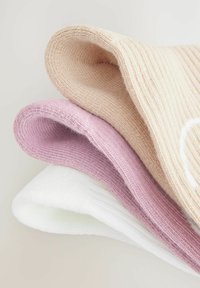Drei Paare Socken in hellen Farbtönen: beige, hellrosa und weiß. Gestreifte Textur und gerollte Bündchen, die den weichen, gestrickten Stoff zur Schau stellen.