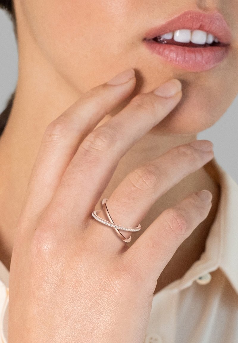 Zlati prstan iz rožnatega zlata z vključenimi trakovi, eden je gladek in eleganten, drugi pa krasijo majhni diamanti v vrsti. Vidna je tudi barva kože.