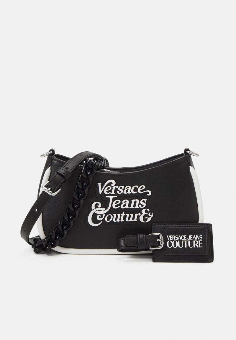 Sac d'épaule Versace Jeans Couture noir et blanc avec texte logo, chaîne noire et sangle en cuir, ainsi qu'une étiquette de bagage assortie avec la marque.