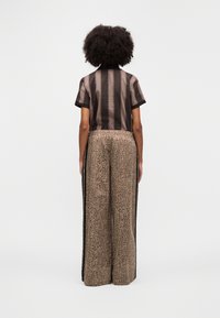 Short-sleeved shirt with brown vertical stripes and matching high-waisted, wide-leg pants featuring a textured animal print and black side stripes.