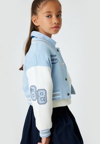 Giacca varsity accorciata blu chiaro con maniche bianche e strisce blu. Presenta testo ricamato e il numero '88' in navy.